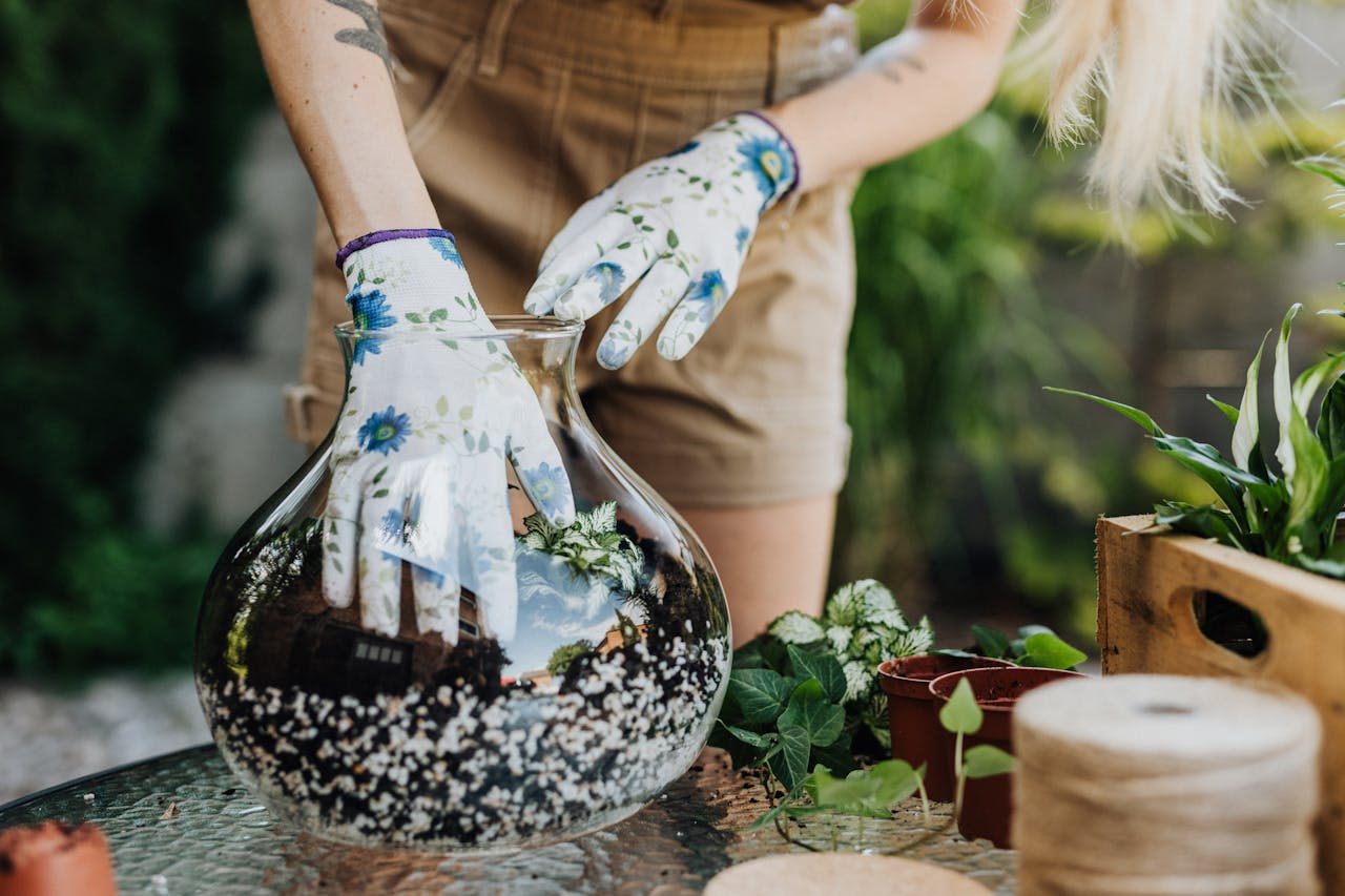 Close-up of a gardeners hands creating a terrarium with diverse plants in a glass vase.